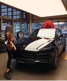 a woman standing next to a black car with a red bow on top