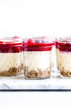 four jars filled with food sitting on top of a white marble counter topped with berries and granola