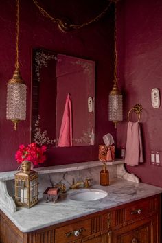 a bathroom with red walls and marble counter tops, gold fixtures and pink towels hanging on the wall