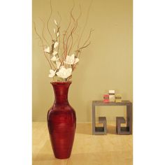 a red vase with white flowers in it on a table next to a side table