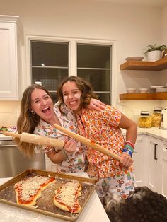 two women in the kitchen with some pizzas and a rolling pan on the counter