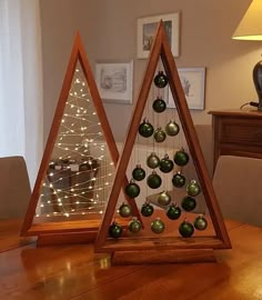 two triangle shaped christmas ornaments sitting on top of a wooden table next to a lamp