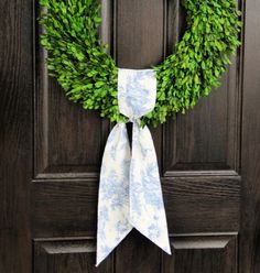 a wreath on the front door with a white bow hanging from it's side