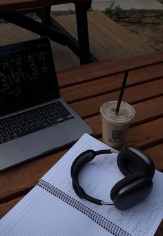 an open notebook with headphones on it next to a coffee cup and laptop computer