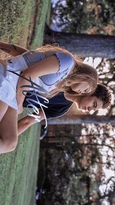 two girls are standing next to each other in front of some water and trees with their hands together