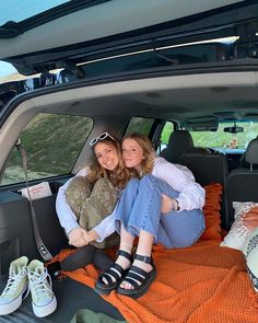 two young women sitting in the back of a car with their feet on the ground