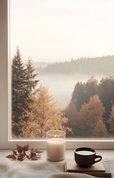 a candle, book and cup sit on a window sill in front of a scenic view