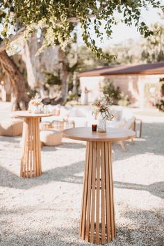 two wooden tables sitting on top of a gravel covered field next to a large tree