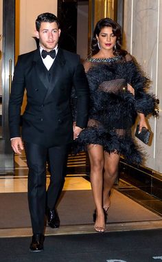 a man and woman dressed in black walking down a hall way with one holding the other's hand