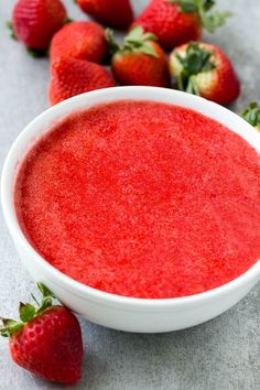 a white bowl filled with red liquid next to strawberries