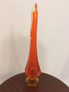 an orange glass vase sitting on top of a wooden table next to a white wall