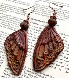 a pair of brown earrings sitting on top of an open book with beads hanging from it