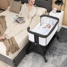 a woman laying on top of a bed next to a baby in a crib