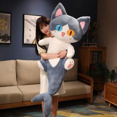 a woman holding a large stuffed cat in her arms while standing next to a couch