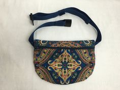 a small blue purse with an ornate design on the front and shoulder strap is shown