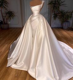 a white wedding dress on display in a room with wood flooring and potted plants