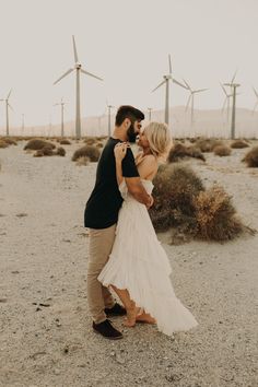 a man and woman standing next to each other in front of windmills