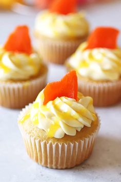 several cupcakes with orange and white frosting on them sitting on a table