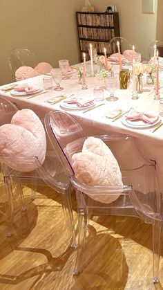 the table is set with clear chairs and pink linens on it, along with candles