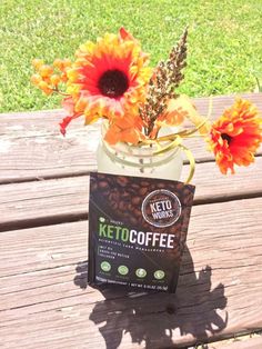 a jar with some flowers in it sitting on a wooden table next to a bag of coffee