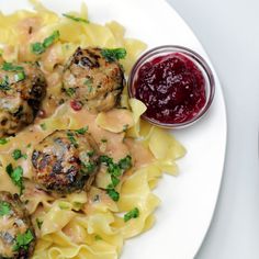 a white plate topped with pasta and meatballs next to a jar of cranberry sauce