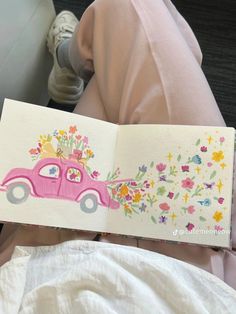 an open book with a drawing of a pink car and flowers on the front cover