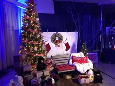 a christmas tree and presents in front of a stage set up for a holiday party