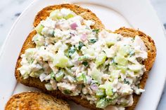 two pieces of bread with chicken salad on them sitting on a plate next to another piece of bread