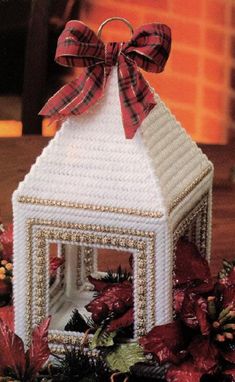 a white house ornament with a red bow on it and pine cones in the background