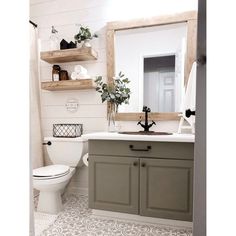 a white toilet sitting next to a bathroom sink under a wooden mirror mounted above it