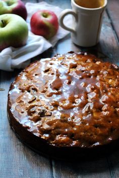 a cake sitting on top of a wooden table next to two mugs and apples