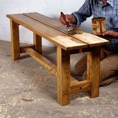 a man sitting on the ground with a paintbrush and brush in his hand next to a wooden bench