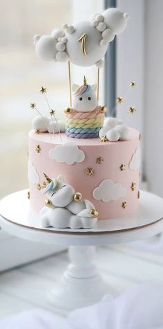 a pink cake with white clouds and a unicorn on top is sitting on a table