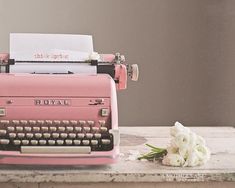 an old pink typewriter sitting on top of a table next to flowers and paper