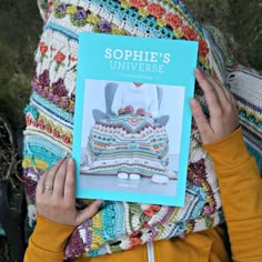 a woman is holding up a book about crochet and the cover shows a multicolored cake