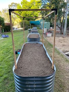 an empty metal barrel filled with dirt in the middle of a yard and some trees