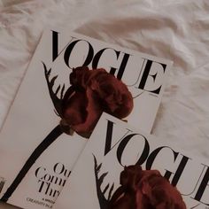 two magazines with red flowers on them laying on a white bed sheet, next to each other