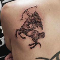 the back of a woman's shoulder with an arrow and horse tattoo on it