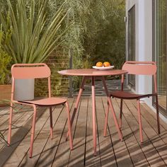 an outdoor table and two chairs on a wooden deck with potted plants in the background