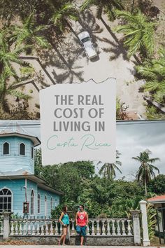 two people standing in front of a blue house with a sign that says the real cost of living in costa rica