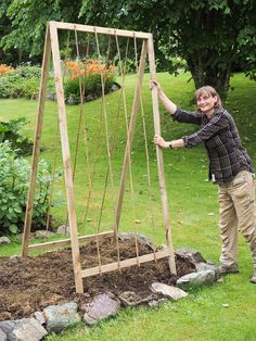 a woman standing next to a wooden trellis on top of a lush green field