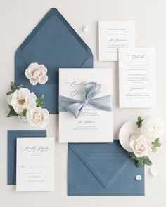 the wedding stationery is laid out on top of blue envelopes and white flowers