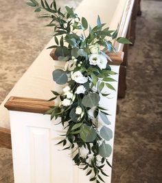 flowers and greenery are on the back of a church pew