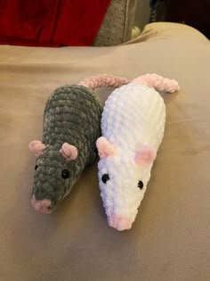 two knitted mice laying on top of a bed next to each other, one white and the other gray