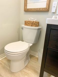 a white toilet sitting in a bathroom next to a wooden cabinet and framed painting on the wall