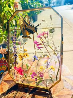 a glass vase filled with flowers on top of a wooden table next to a potted plant