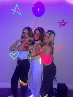 three girls are posing for the camera with neon lights on their faces and arms, in front of a purple background