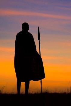 the silhouette of a man holding a spear and standing in front of an orange sky