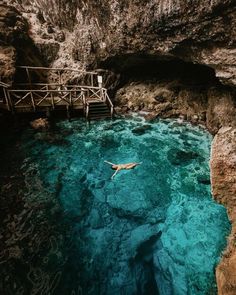 a person swimming in the blue water near a wooden bridge and some steps leading up to it