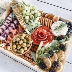 a platter filled with cheese, crackers, grapes and meats on a wooden tray